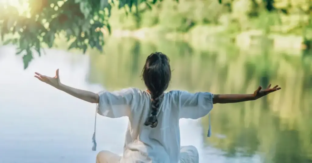 donna di spalle con le braccia aperte al cielo con nello sfondo uno specchio di acqua | Corpo e anima