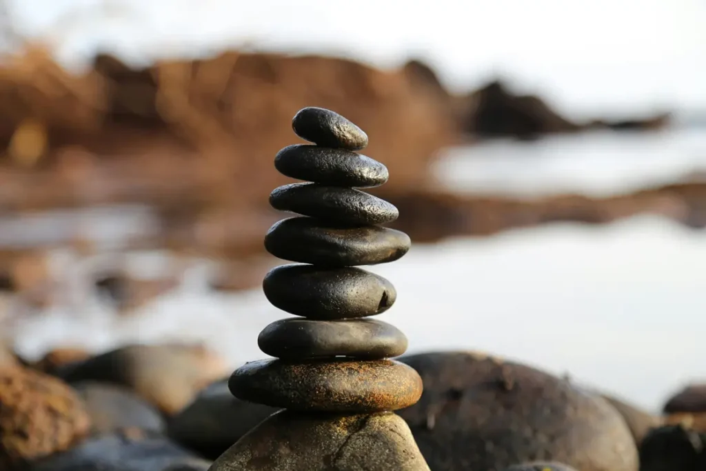 Pietre impilate una sull'altra in spiaggia, simbolo di equilibrio interiore e libertà emotiva per superare la dipendenza affettiva | Corpo e anima
