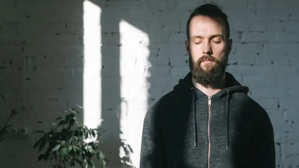 Uomo in posizione meditativa con gli occhi chiusi e un raggio si luce in volto | Corpo e anima