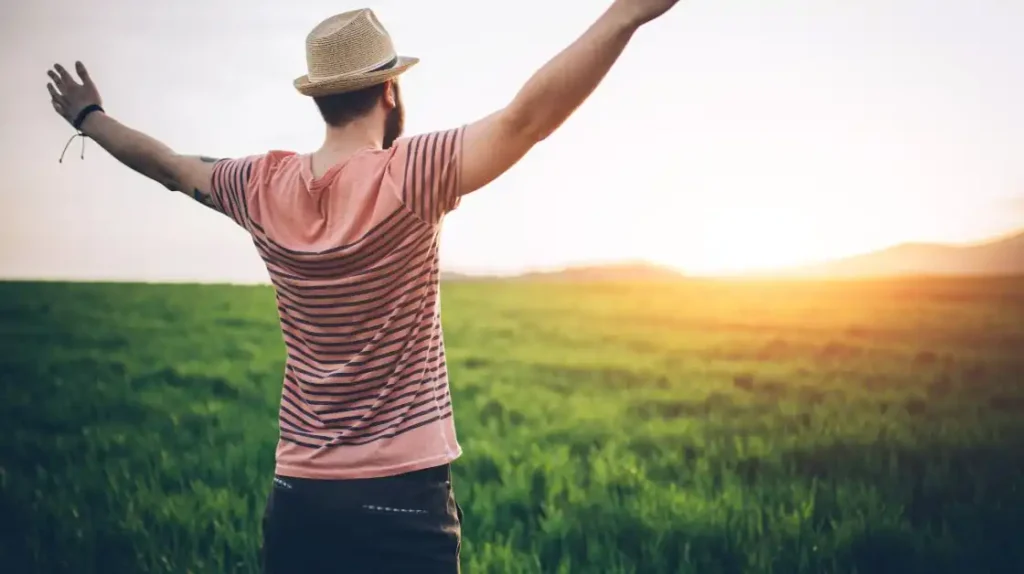 Un uomo di spalle con le braccia aperte e alzate al cielo con una luce soffice dell'alba | Corpo e anima