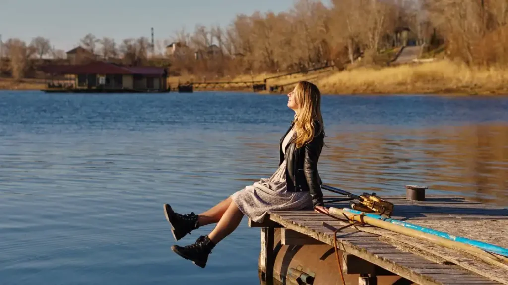 radicamento spirituale di una donna seduta su un pontile con gli occhi chiusi e il volto al sole che la bacia | Corpo e anima