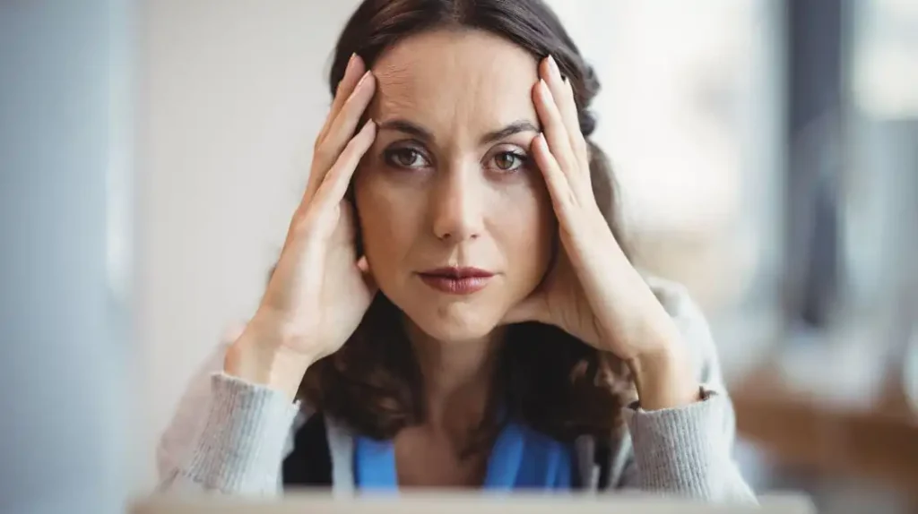 Terapia reichiana come funziona: donna con le mani sul volto e lo sguardo stanco e imprigionato | Corpo e anima